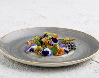 Piatto gourmet con fiori commestibili e ingredienti raffinati.