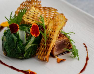 Piatto gourmet con patate croccanti, verdure e decorazioni floreali.