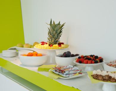 Buffet with fresh fruit, snacks, and various sweets on a white table.