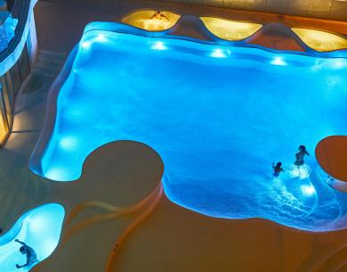 Beleuchteter Pool bei Nacht mit schwimmenden Personen.