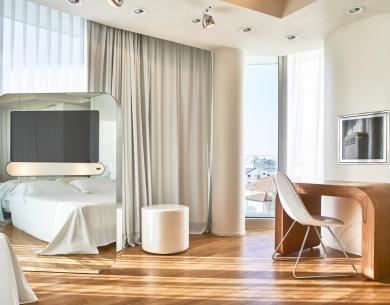 Modernes Zimmer mit Bett, Schreibtisch und großen Fenstern.