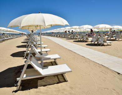 Beach with white umbrellas and loungers on golden sand under blue sky.