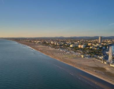 Plage au coucher du soleil, mer calme, ville animée à l'horizon.