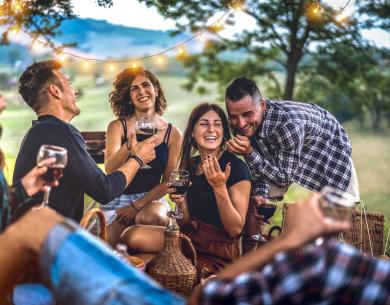 Amici che si divertono all'aperto con vino e luci decorative.