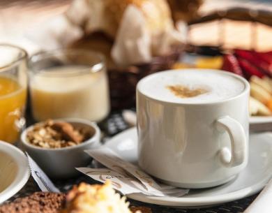 Colazione con cappuccino, succo, dolci e cereali in un cestino.