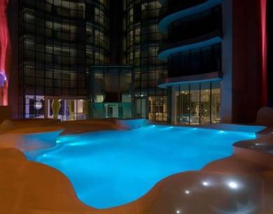 Piscina illuminata di notte in un moderno edificio con ampie vetrate.
