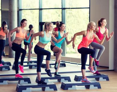 Group of women doing step aerobics in a bright gym.