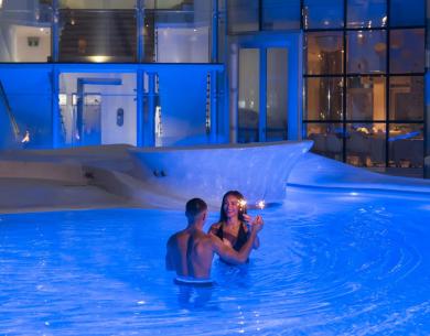 Romantisches Paar im blau beleuchteten Pool, magischer Abend.