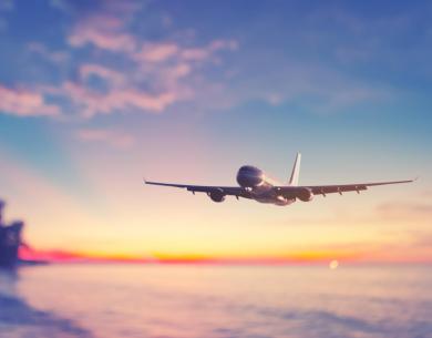 Flugzeug fliegt bei Sonnenuntergang über ruhiges Meer, bunter Himmel berührt.
