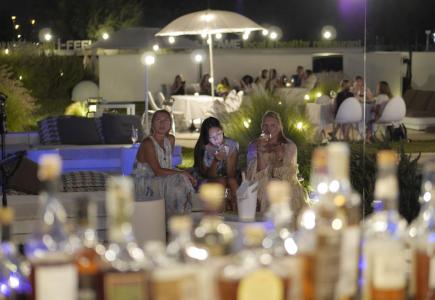 Serata estiva, donne rilassate, atmosfera elegante con luci soffuse e drink.