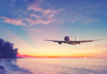 Flugzeug fliegt bei Sonnenuntergang über ruhiges Meer, bunter Himmel berührt.