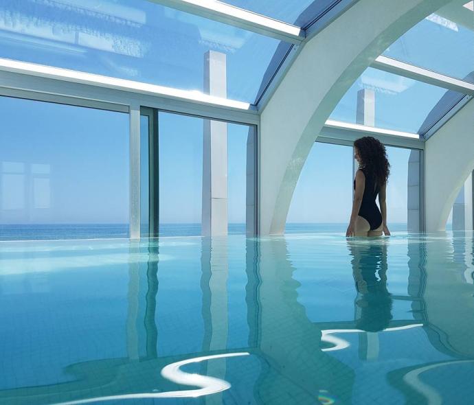 Femme dans une piscine intérieure avec vue sur la mer.