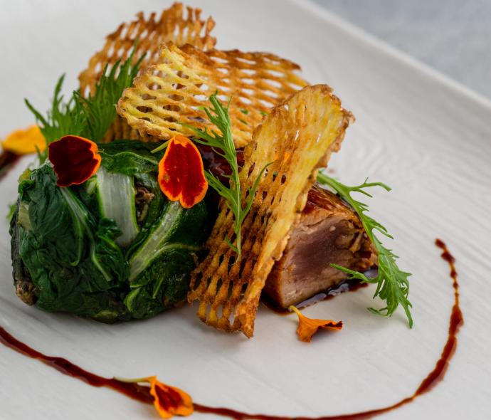 Piatto gourmet con patate croccanti, verdure e decorazioni floreali.