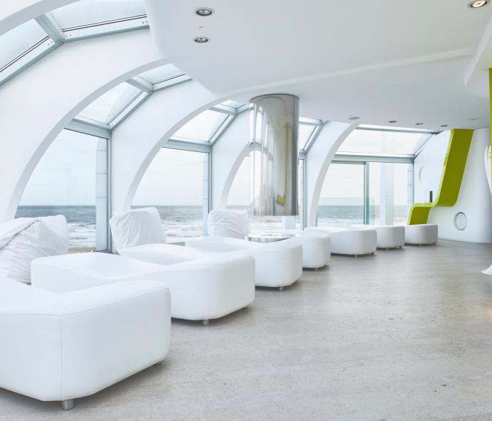Sala relax moderna con vista mare, arredamento bianco e dettagli verdi.