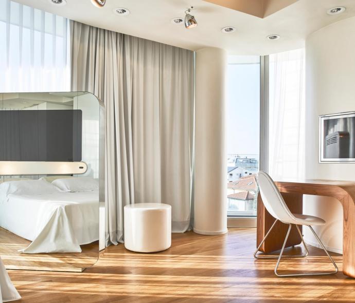 Modernes Zimmer mit Bett, Schreibtisch und großen Fenstern.