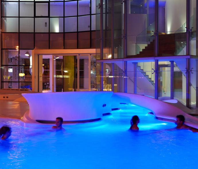 Beleuchteter Pool bei Nacht mit schwimmenden Personen.