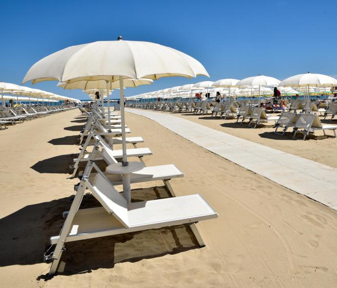 Beach with white umbrellas and loungers on golden sand under blue sky.