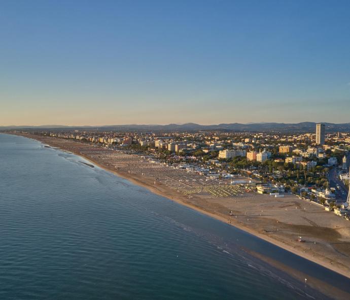 Plage au coucher du soleil, mer calme, ville animée à l'horizon.