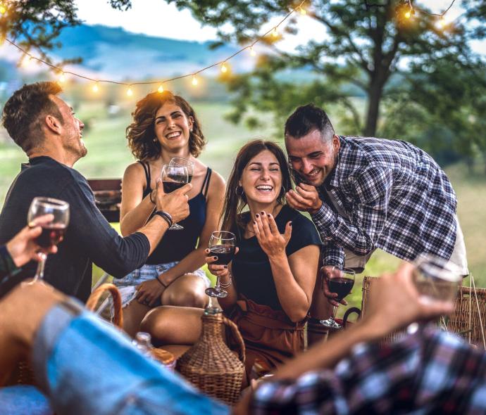 Amici che si divertono all'aperto con vino e luci decorative.