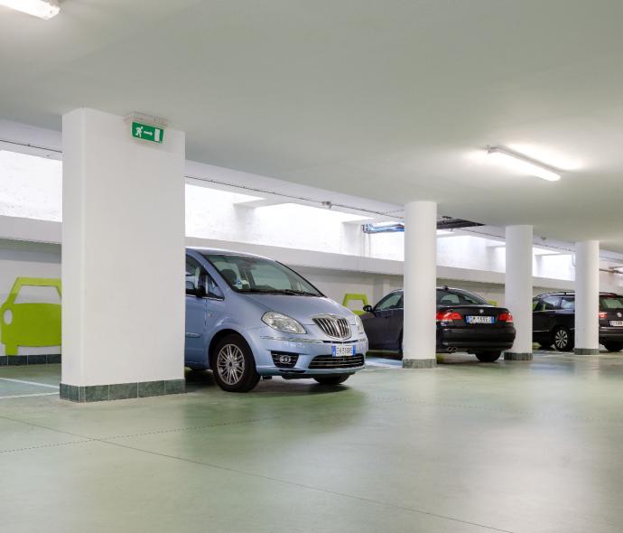 Parcheggio sotterraneo con auto e segnaletica verde.