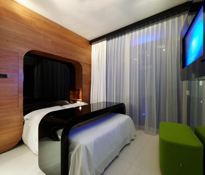 Camera moderna con letto, TV e sedute verdi.