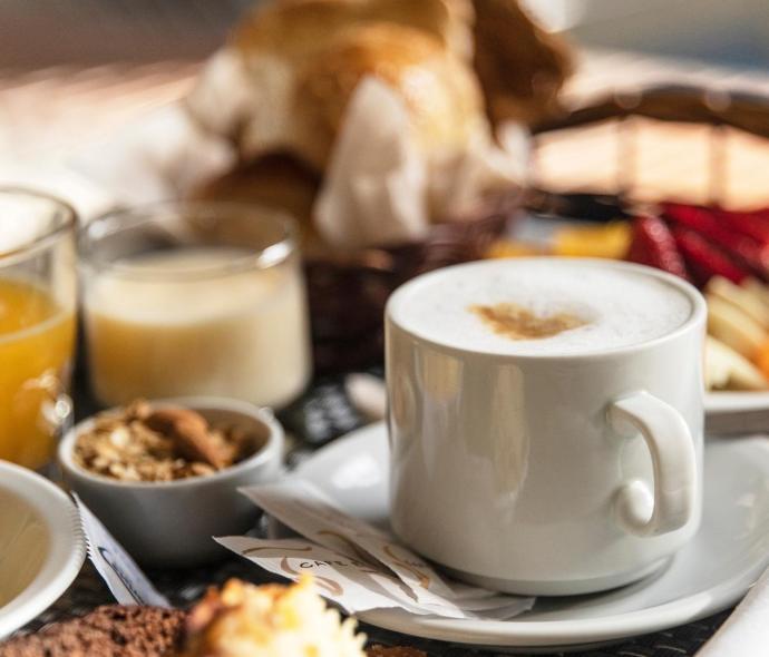Colazione con cappuccino, succo, dolci e cereali in un cestino.