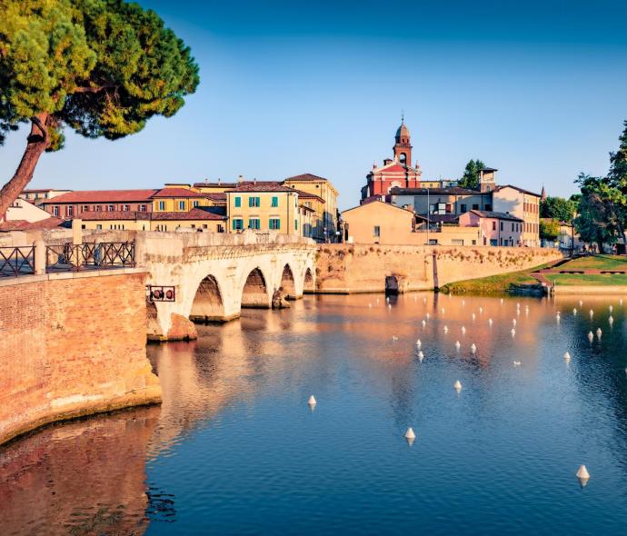 Historische Brücke über einen Fluss, umgeben von bunten Gebäuden und Bäumen.