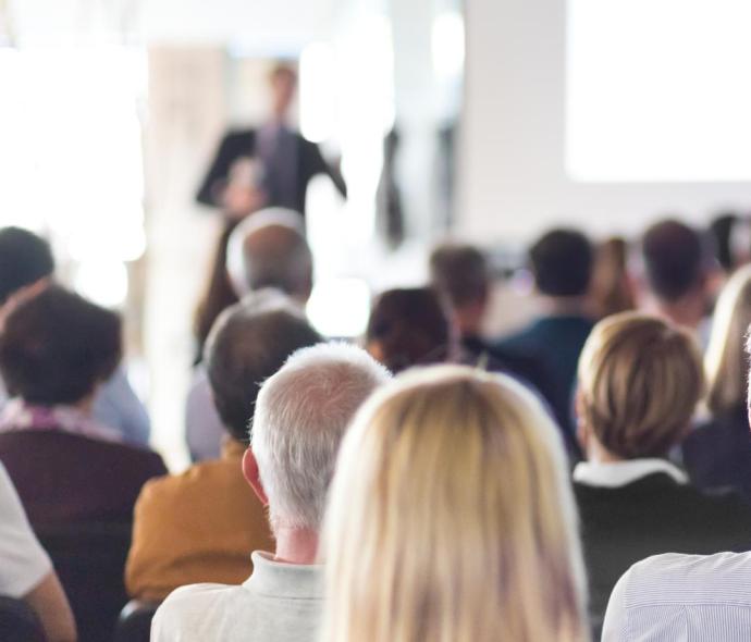 Persone sedute ascoltano una presentazione in una sala conferenze.