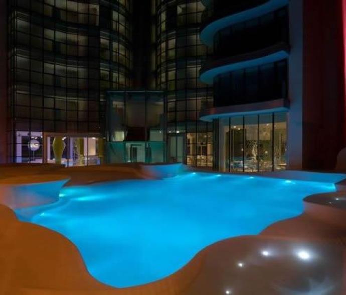 Piscina illuminata di notte in un moderno edificio con ampie vetrate.
