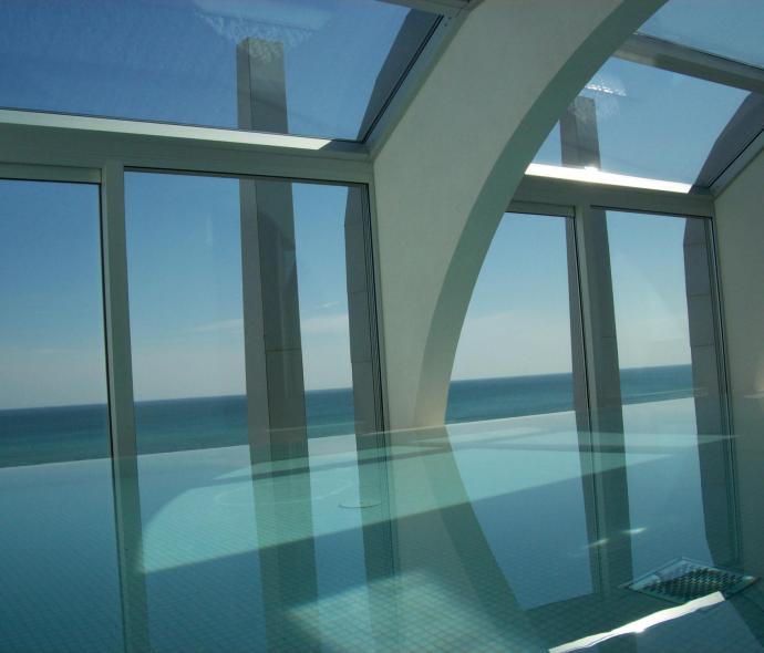 Piscina interna con vista mare, ampie finestre e arcate bianche.