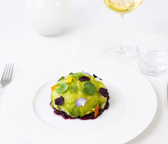 Piatto gourmet con foglie e fiori, accompagnato da vino bianco.