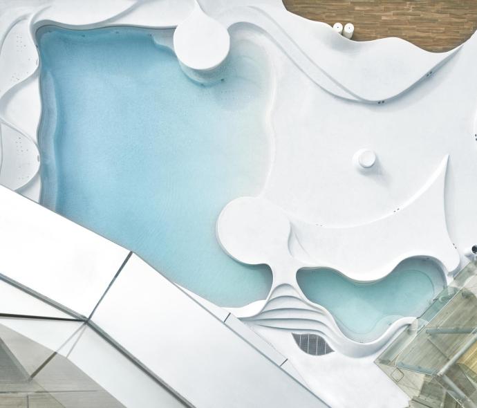 Piscina moderna con design ondulato e strutture in vetro.