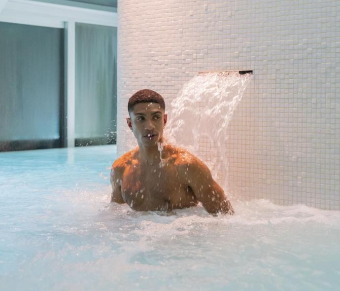 Man in a pool under a waterfall.