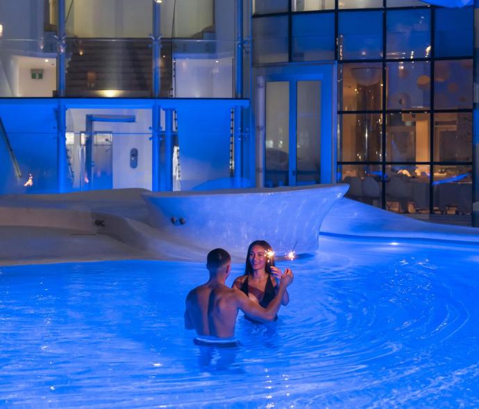 Romantisches Paar im blau beleuchteten Pool, magischer Abend.