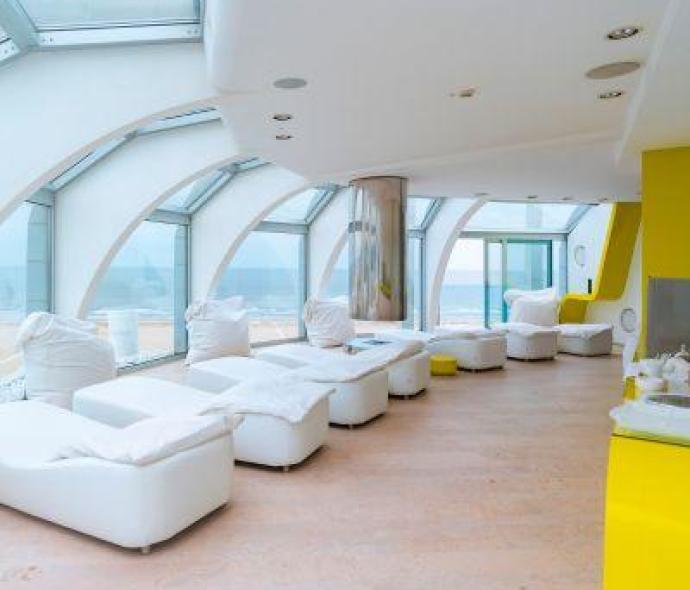 Heller Entspannungsraum mit weißen Liegen und Panoramafenstern.
