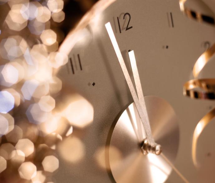 Orologio che segna mezzanotte con luci scintillanti sullo sfondo.