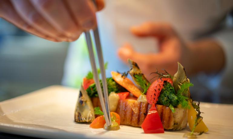 Chef prepara piatto gourmet con pinzette.