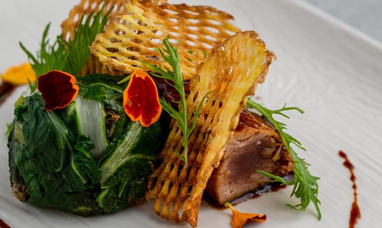 Gourmetgericht mit knusprigen Kartoffeln, Gemüse und Blumendekorationen.