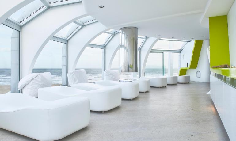Sala relax moderna con vista mare, arredamento bianco e dettagli verdi.
