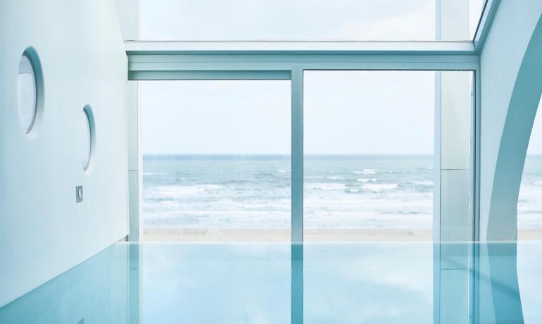 Indoor pool with ocean view through large windows.