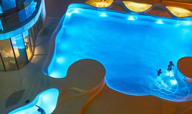 Illuminated pool at night with people swimming.