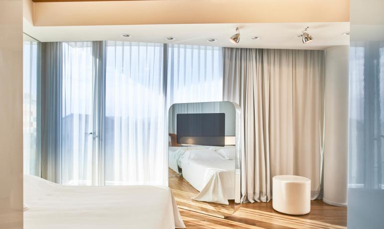 Chambre lumineuse avec rideaux blancs, mobilier moderne et sol en bois.