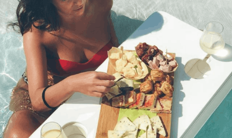 Donna in piscina con tavolo galleggiante e cibo.