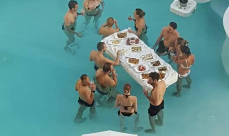 Persone che mangiano e bevono in una piscina con tavolo galleggiante.