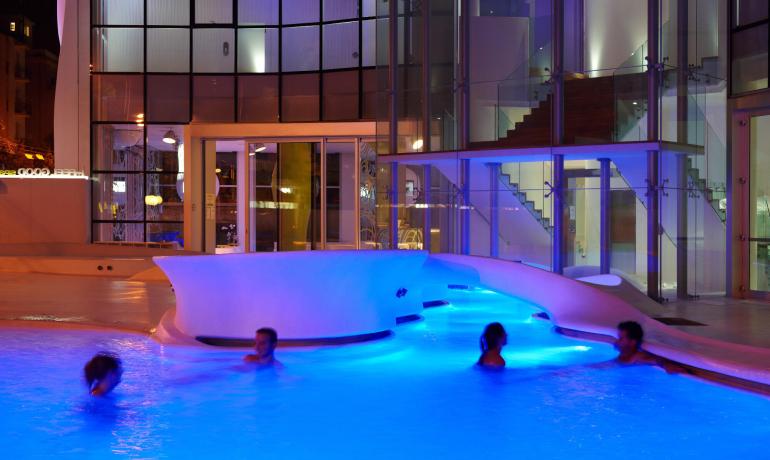 Piscina illuminata di notte con persone che nuotano.