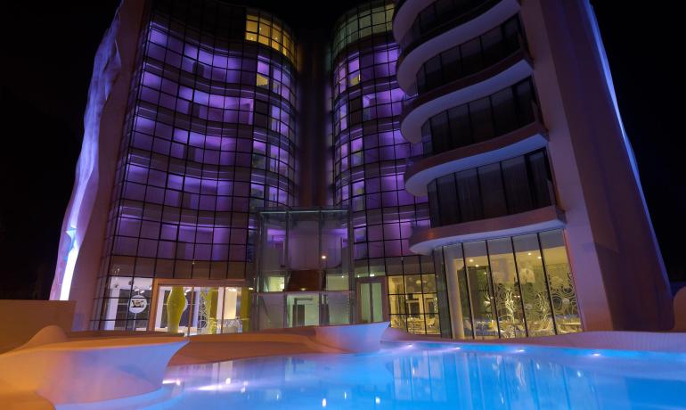 Edificio moderno illuminato di viola, riflesso in una piscina notturna.