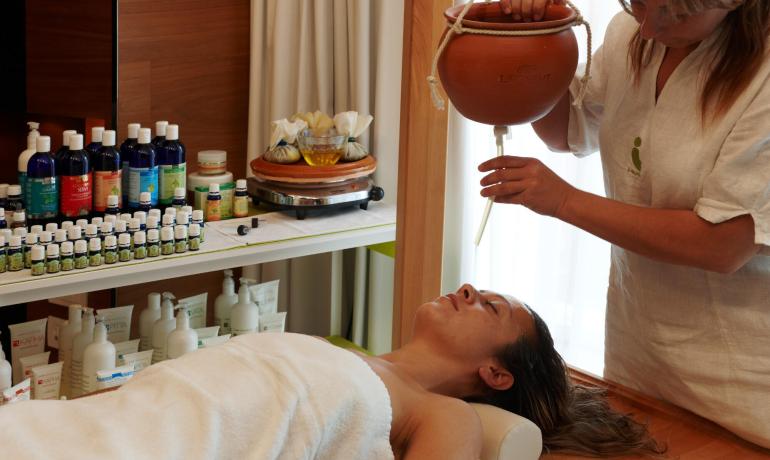 Trattamento ayurvedico con oli essenziali su una donna distesa.
