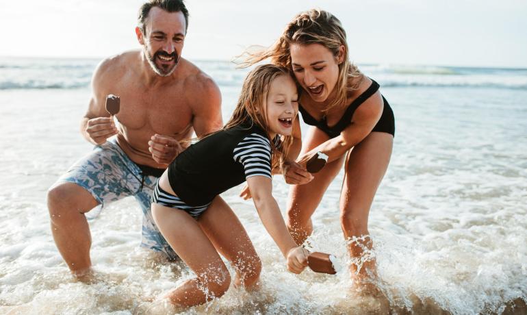 Happy family plays in the sea with popsicles, smiles, and splashes.