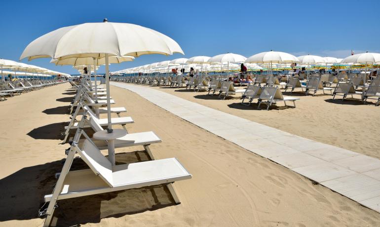 Strand mit weißen Sonnenschirmen und Liegen auf goldenem Sand unter blauem Himmel.