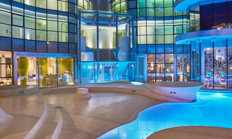 Piscina futuristica illuminata con edificio moderno di vetro.